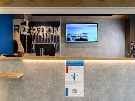 A reception desk with a monitor displaying a welcome message, a sign with a QR code, and a blue wall with a partial view of a mannequin.