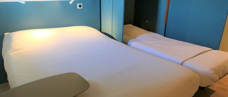 Una habitación de hotel con cama, mesita de noche y lámpara de pared.