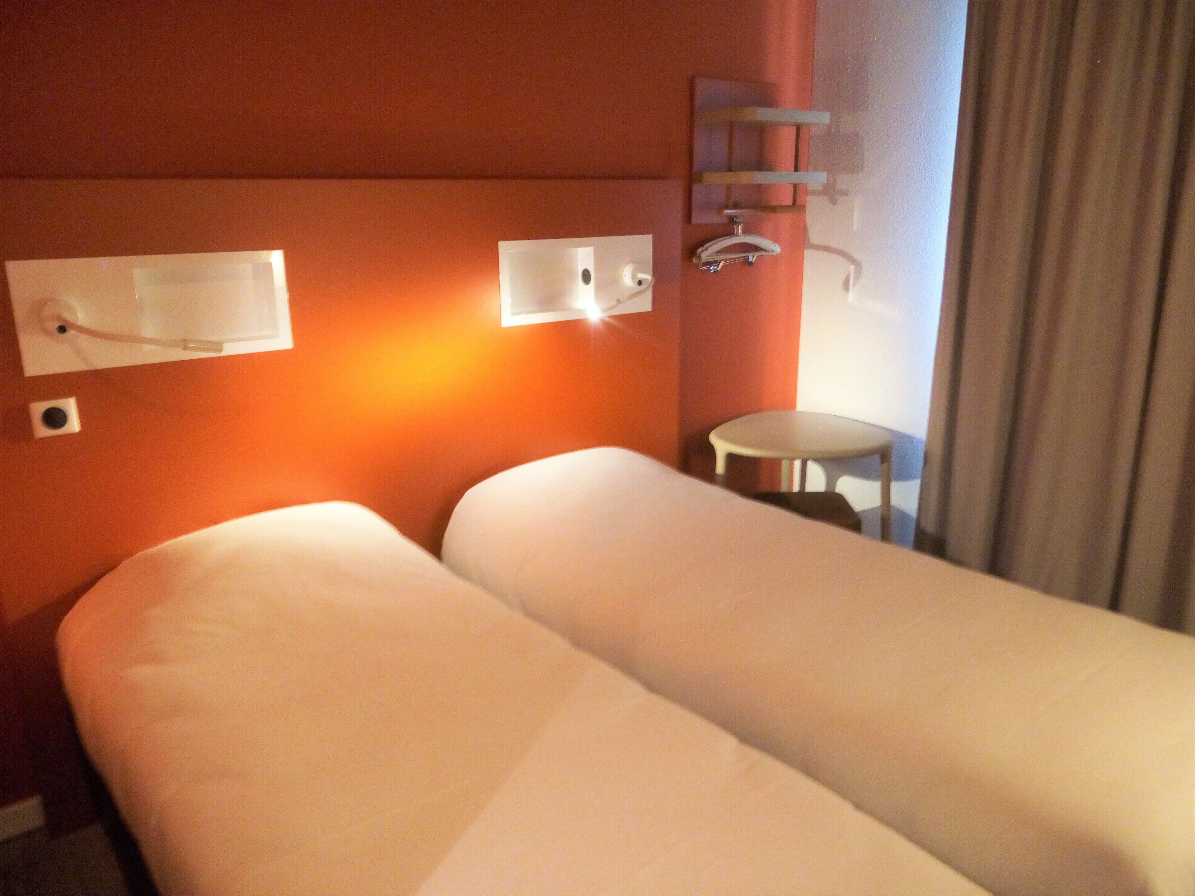 A hotel room with a bed, a small table, and a wall-mounted light fixture.