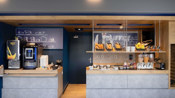 A coffee shop counter with a coffee machine, a menu board, and various food items displayed. - Ibis Budget Perigueux Boulazac (Boulazac-Isle-Manoire)