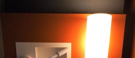 Un coin de pièce avec un bureau en bois, une lampe fixée au mur, une télécommande et un haut-parleur.