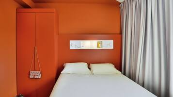 Ein Schlafzimmer mit oranger Wand, einem weißen Bett, einem grauen Vorhang und einer hängenden Tasche.