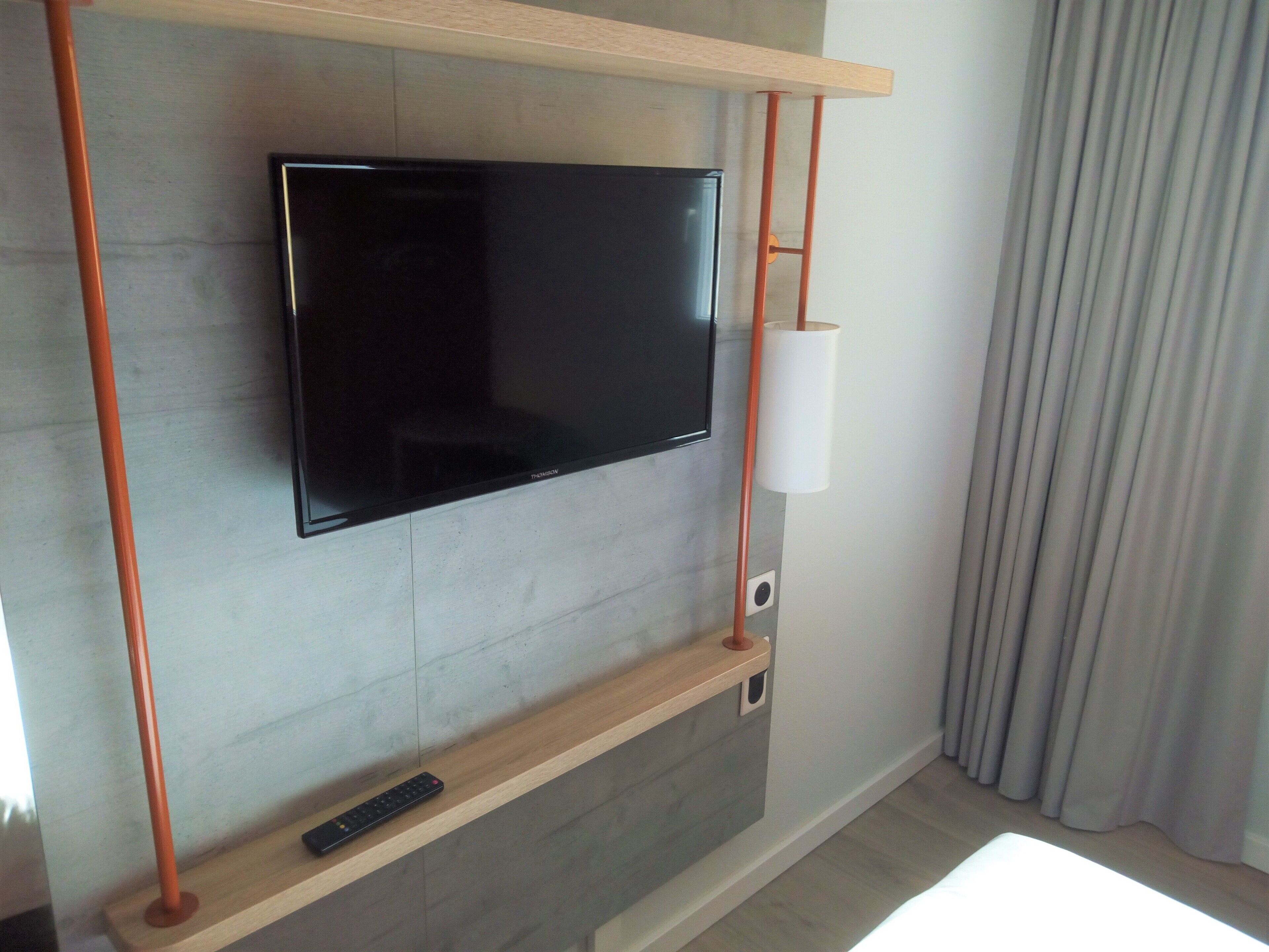 Un téléviseur à écran plat fixé au mur, avec une étagère en bois en dessous.