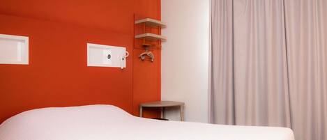 Una habitación de hotel con cama, una mesita, un perchero y una ventana con cortinas.