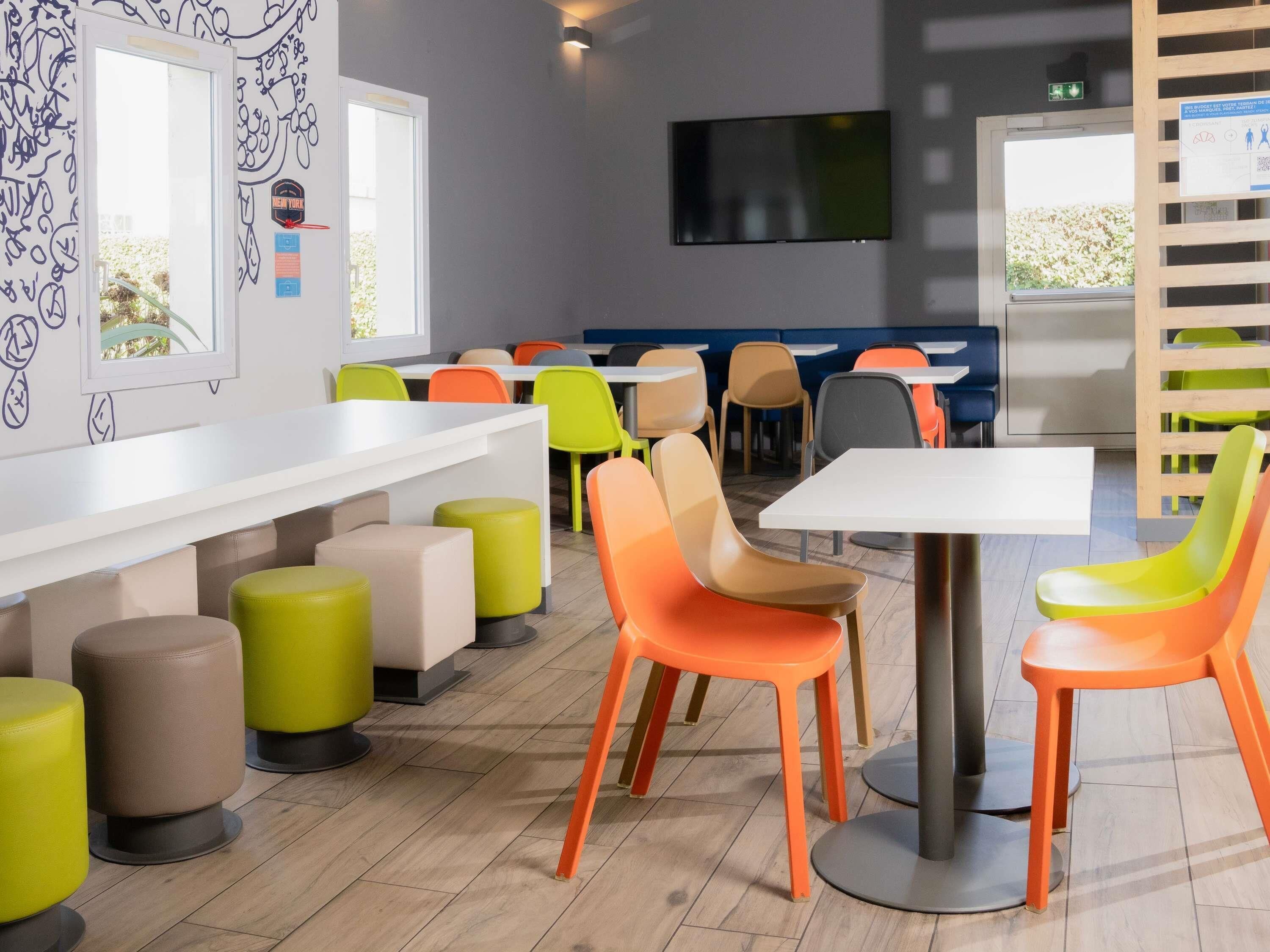 A modern dining area with high tables and colorful chairs, a flat-screen TV, and a window with a view.