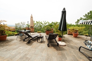A patio with outdoor furniture, potted plants, and a view of the sea. - Felicin - Villa Stella (Monforte d'Alba)