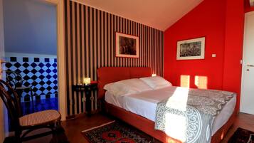 Una camera da letto con una parete rossa, un letto con lenzuola bianche, un motivo a righe sulla parete e una sedia.