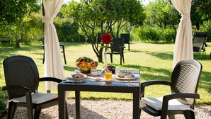 Een buitentafel met stoelen, een fruitmand en een vaas met een rode bloem.