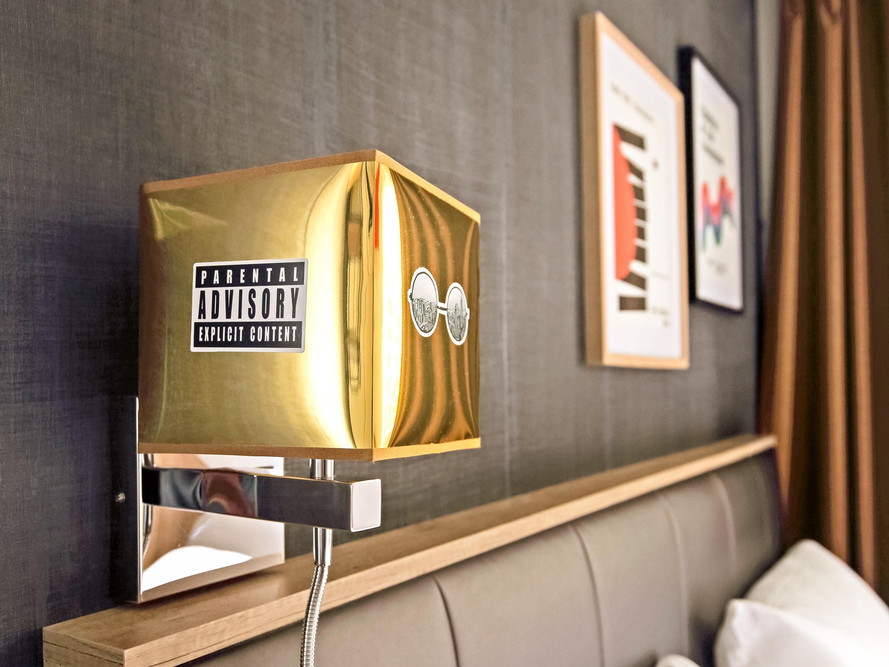 A hotel room with a bed, a bedside table, and a wall-mounted alarm clock.