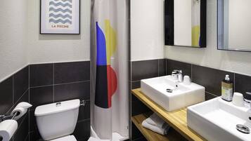 Un baño moderno con inodoro blanco, cortina de ducha con diseño colorido, lavamanos con espejo y un cuadro enmarcado en la pared.