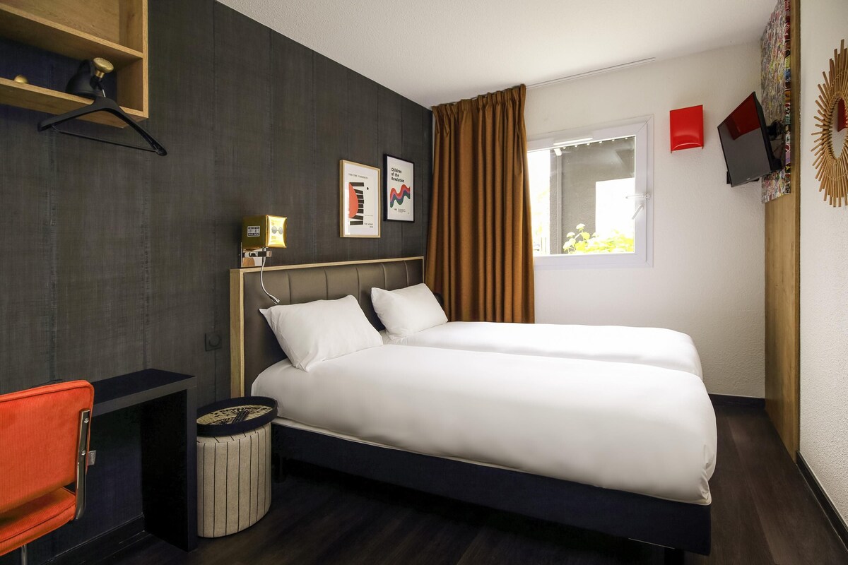 A modern hotel room with a large bed, a desk, a chair, and a small round table.