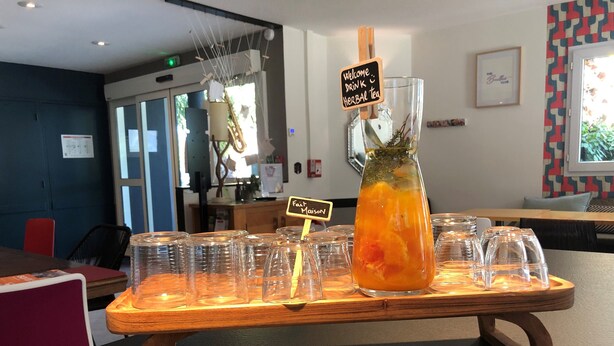 Un espace bar avec un comptoir en bois, une grande carafe de thé aux herbes et plusieurs verres alignés sur le comptoir.