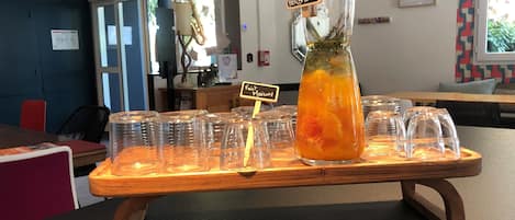 Un espace bar avec un comptoir en bois, une grande carafe de thé aux herbes et plusieurs verres alignés sur le comptoir.