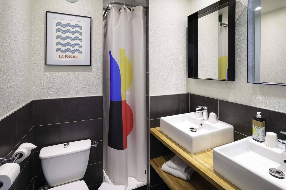 Een moderne badkamer met een wit toilet, een douchegordijn met een kleurrijk ontwerp, een wastafel met een spiegel erboven en een lijst met een foto aan de muur.