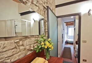 A bathroom with a stone wall, a wooden vanity, and a mirror. There is a vase with yellow flowers on the vanity.