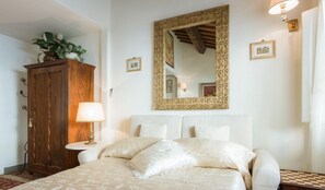 A bedroom with a bed, a wooden cabinet, a lamp, a mirror, and framed pictures on the wall.