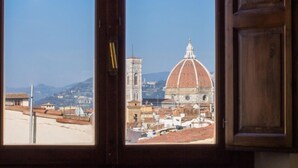 A view through an open door of a building with a large dome and a bell tower in the background. - Florentapartments - Santo Spirito (Florence)