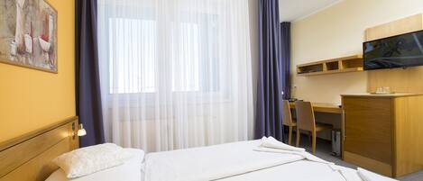 A hotel room with a bed, a desk, a chair, a television, and a painting on the wall.