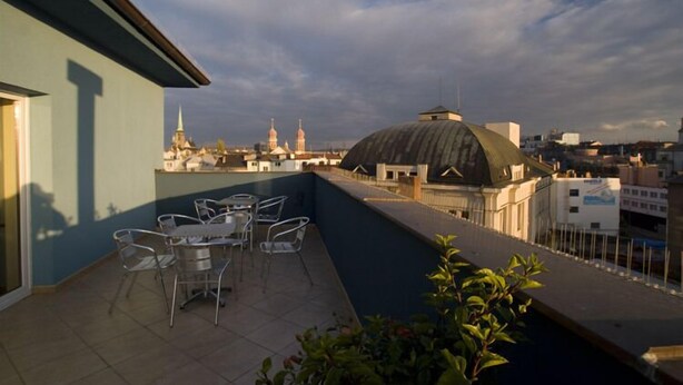 A rooftop terrace with a table and chairs, overlooking a cityscape with domed buildings and a church spire.