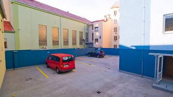 Un área de estacionamiento con una furgoneta roja y un coche azul, junto a un edificio de fachada azul y verde.