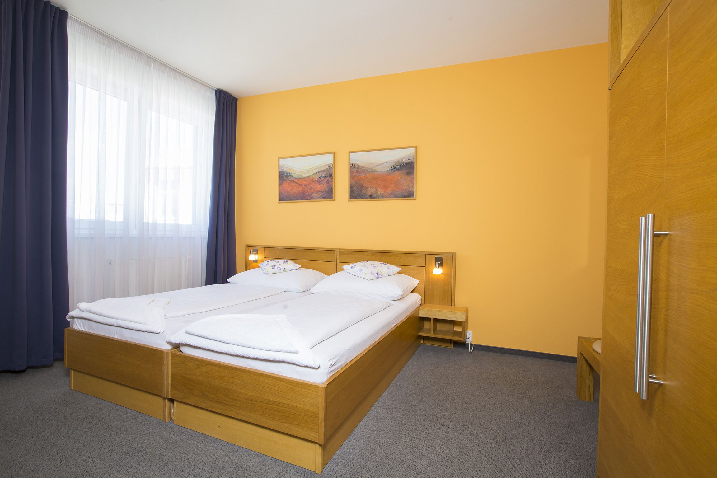 Una cama doble con cabecera de madera, una mesita de noche y dos cuadros colgados en la pared.