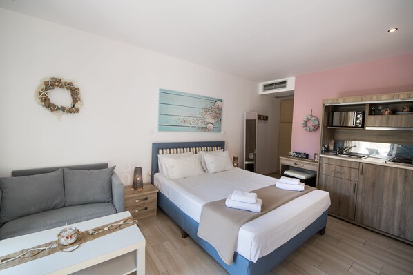A modern bedroom with a bed, bedside table, and a small seating area. - Ilianthos Apartments & Studios (Lefkada)