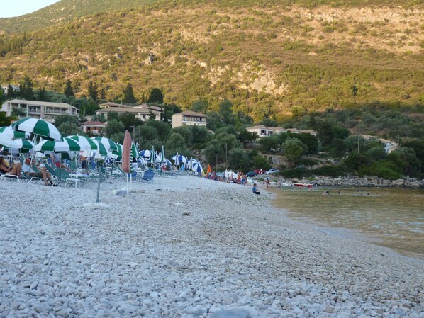 Una playa de guijarros con sombrillas y gente.