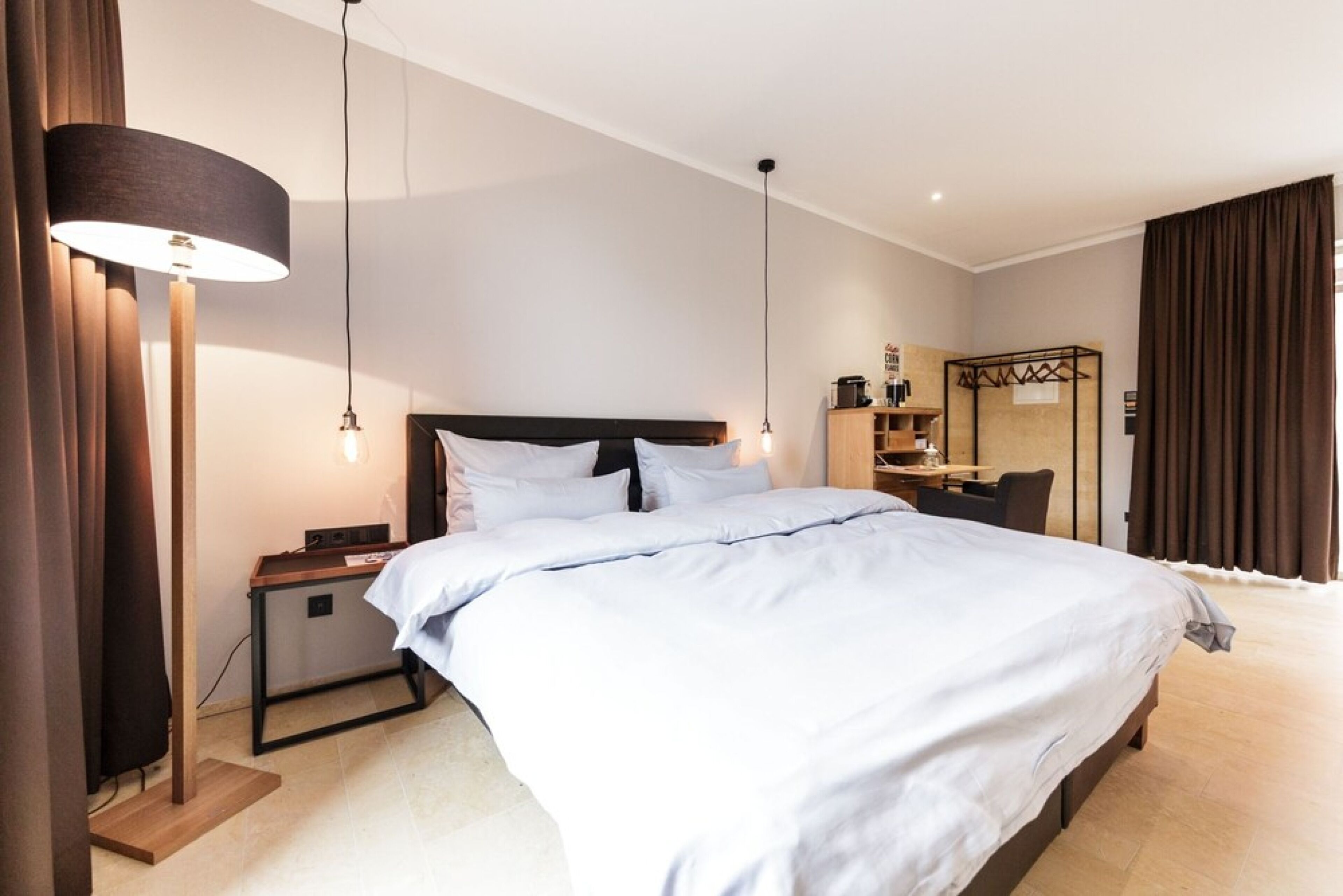 Una habitación de hotel con una cama grande, mesitas de noche, un escritorio, una silla, un armario y una lámpara de pie.