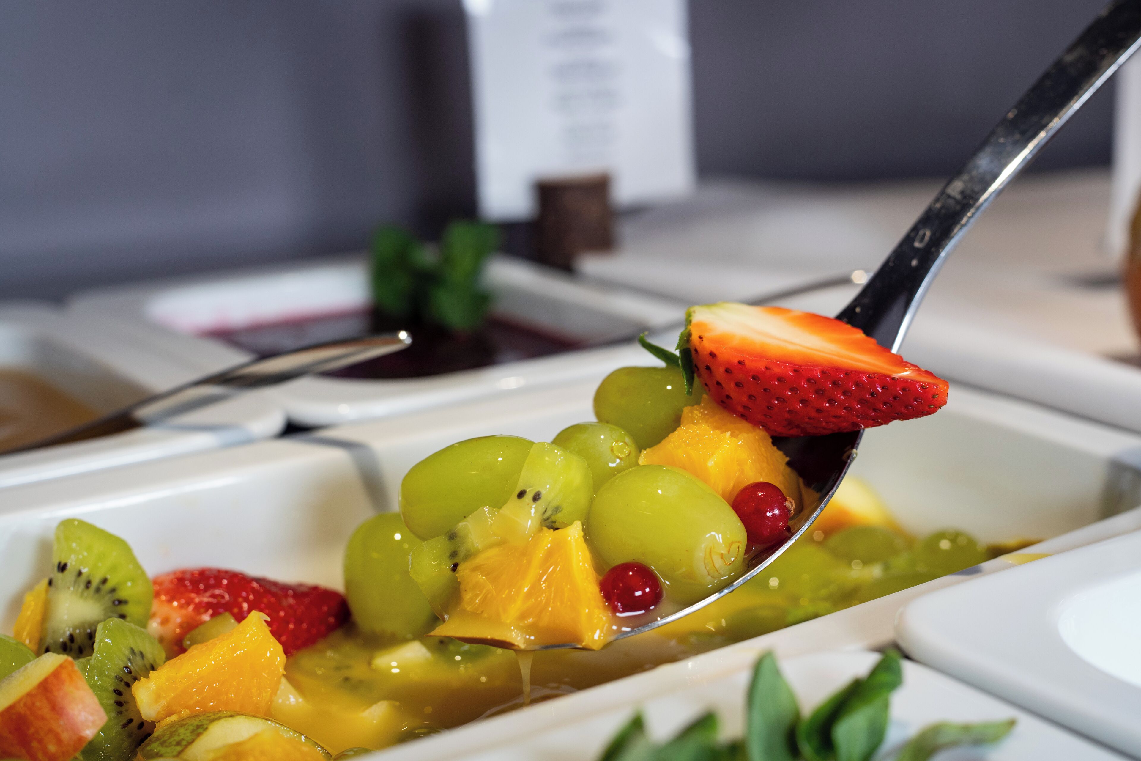 Een detail van een schaal met fruit, inclusief aardbeien, druiven en kiwi, met een lepel vol fruit.