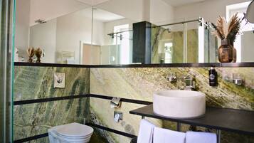 A modern bathroom with a marble wall, a round sink, a toilet, and a glass shower enclosure.