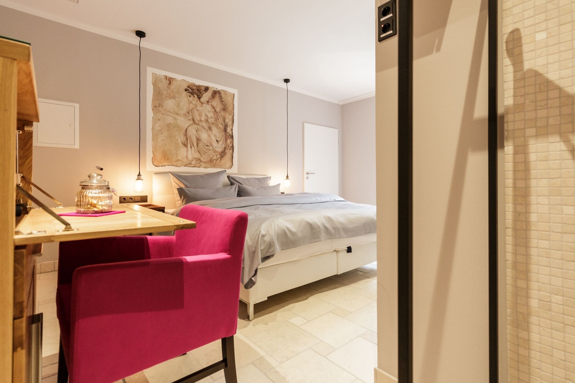A bedroom with a bed, a desk, a chair, and a large painting on the wall.
