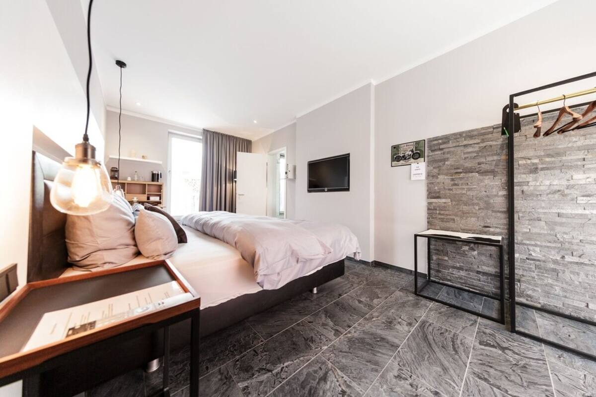 Un dormitorio moderno con cama, mesita de noche y televisor montado en la pared.