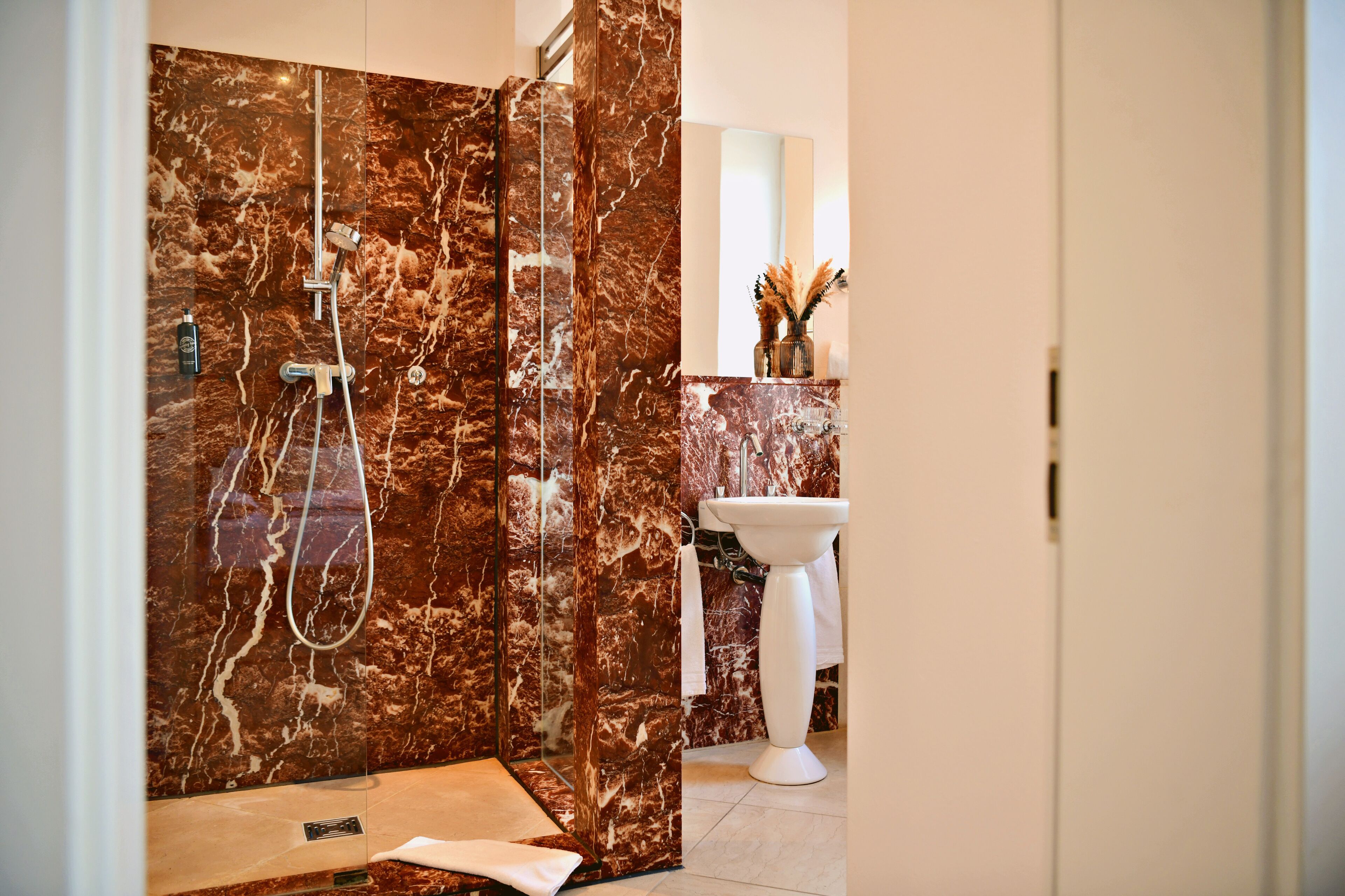 Une salle de bain avec une douche, un lavabo et un mur en marbre.