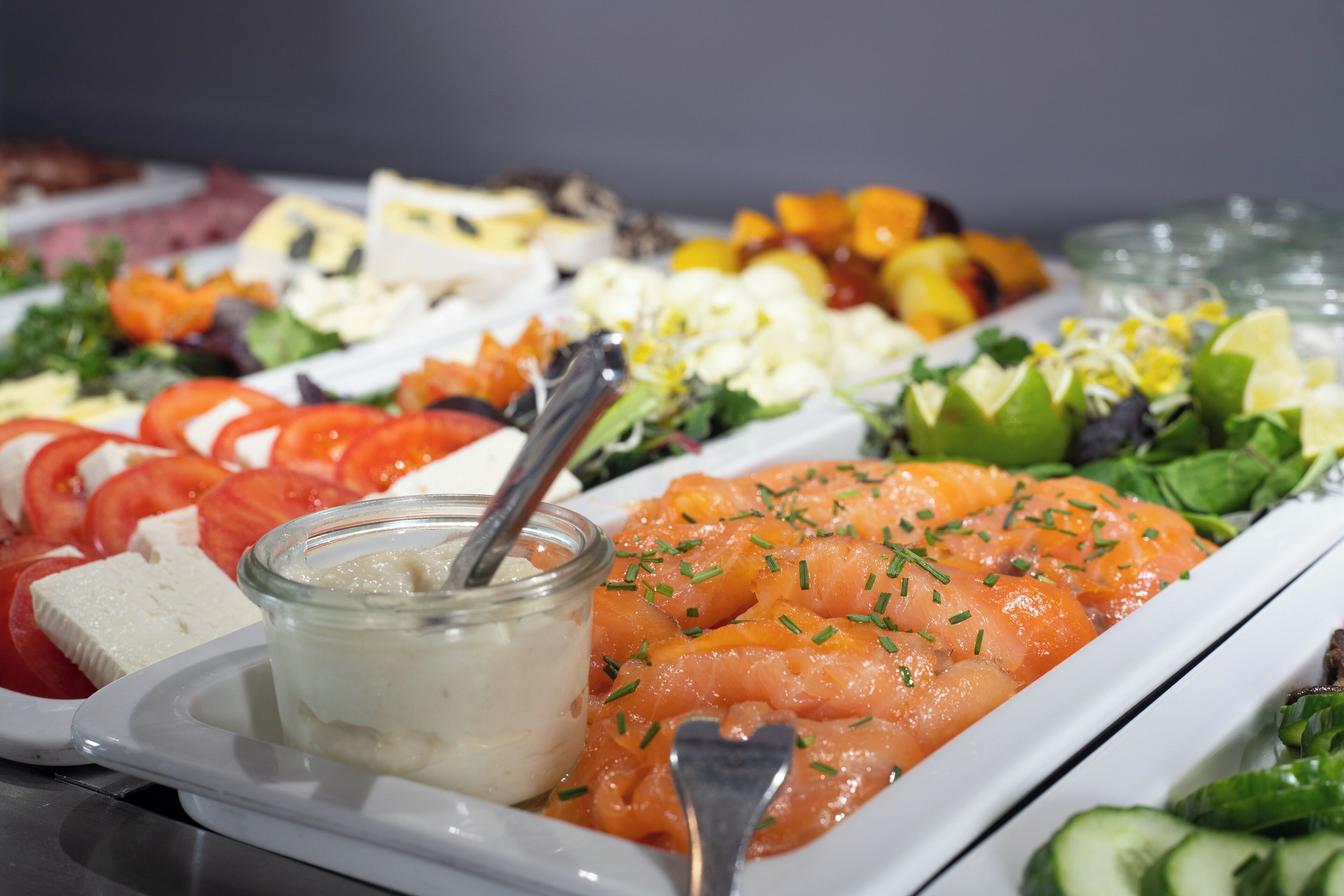 A buffet with various food items including salmon, cheese, and vegetables.