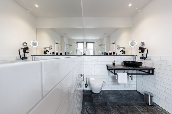 Un baño moderno con un espejo grande, dos lavamanos, una bañera y un inodoro.