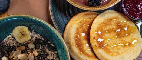 Un desayuno con tortitas, un tazón de cereal con nueces y semillas, y un frutero con diversas bayas y una rodaja de plátano.