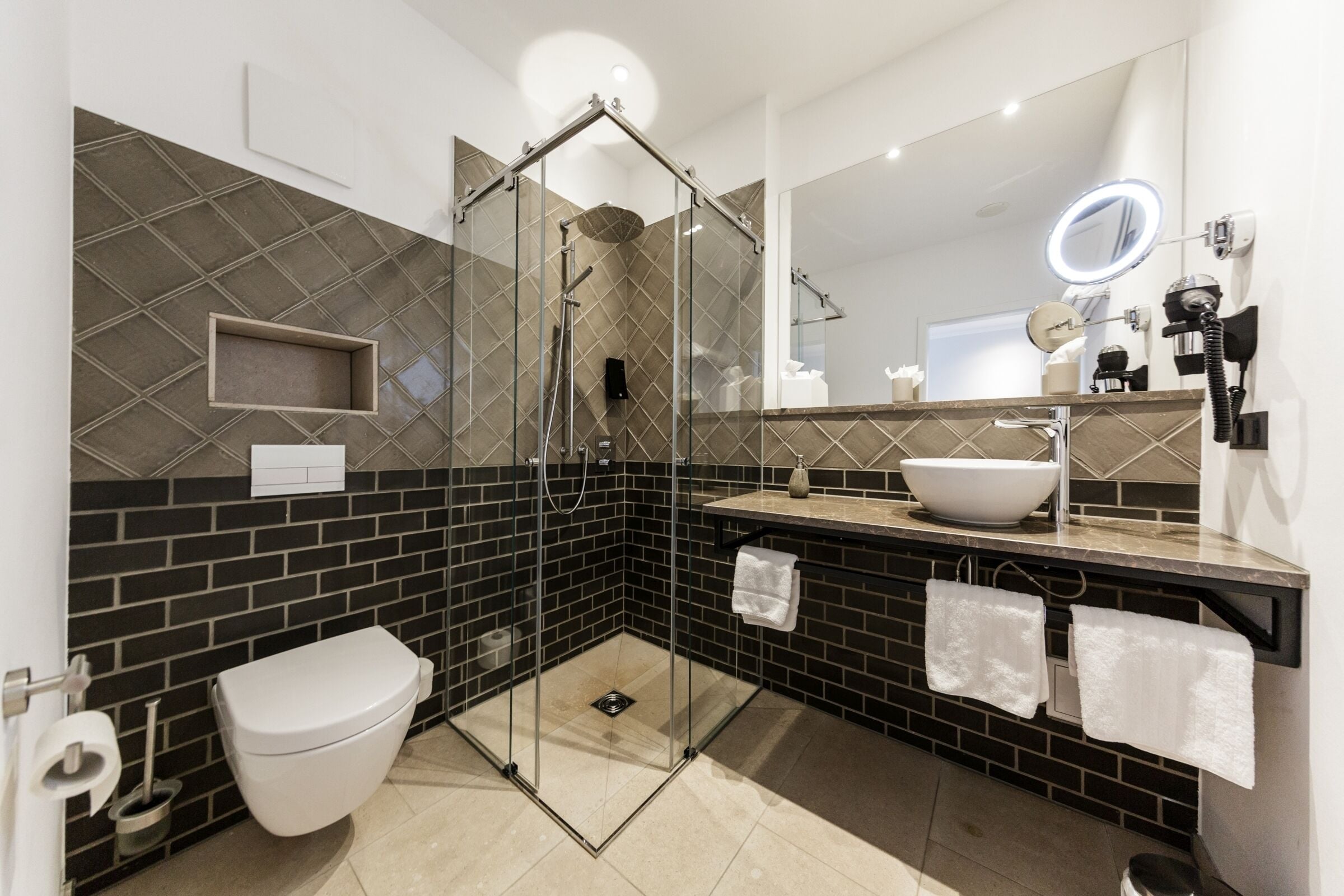 Een moderne badkamer met een douchecabine van glas, een wit toilet, een wastafel met een bijzondere waskom en een spiegel met ingebouwde verlichting.