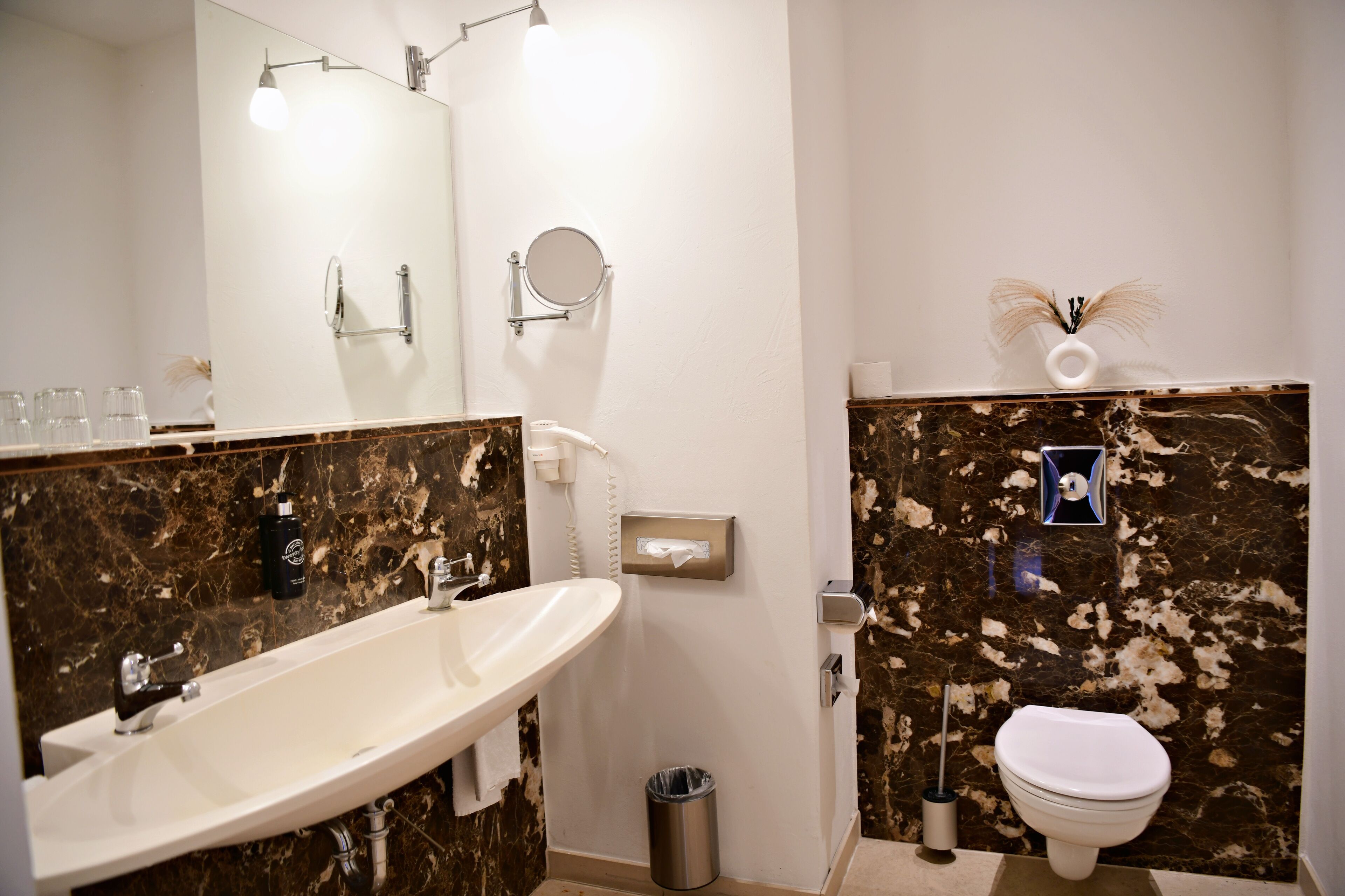 A bathroom with a white sink, a toilet, a mirror, and a trash can.