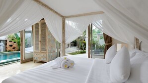 A bedroom with a large bed, white linens, and a canopy. There is a view of a pool and outdoor area with greenery. - Adinda Balangan Beach Villa (Jimbaran)