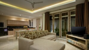 A modern living room with a sofa, TV stand, and kitchen area. - Adinda Balangan Beach Villa (Jimbaran)