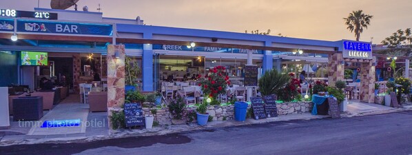 A bar with outdoor seating, a TV screen, and a sign indicating a cocktail bar. - Sunshine (Kos)