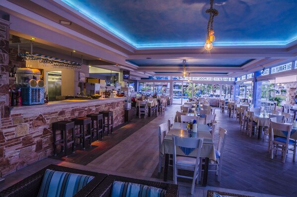 A spacious restaurant with a bar area, multiple seating options, and a view of the outdoors. - Sunshine (Kos)