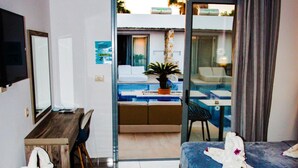 Ett hotellrum med en säng, ett skrivbord, en stol, en TV och en balkong med en pool.