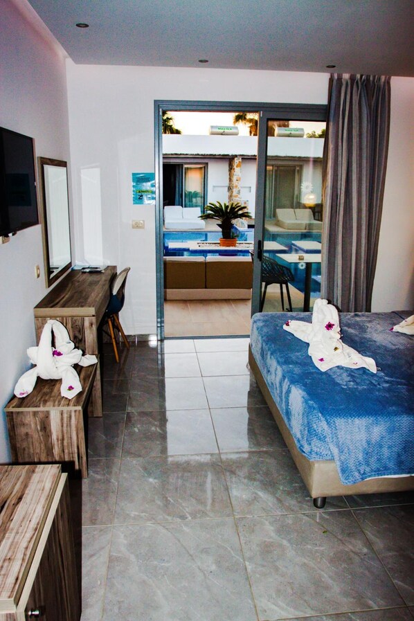 A hotel room with a bed, a desk, a chair, a TV, and a balcony with a pool. - Sunshine (Kos)