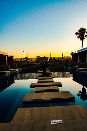 Una piscina con vistas despejadas a la puesta de sol, escalones de piedra que bajan al agua y una palmera a la derecha.