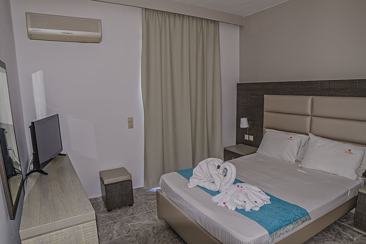 A hotel room with a bed, a TV, a desk, and a window with curtains.