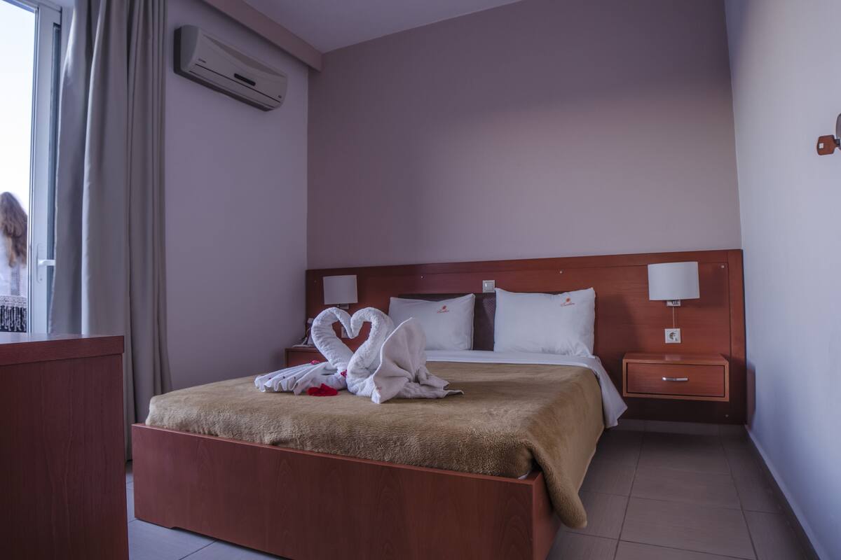 A hotel room with a bed, a nightstand, a lamp, and a window with curtains.