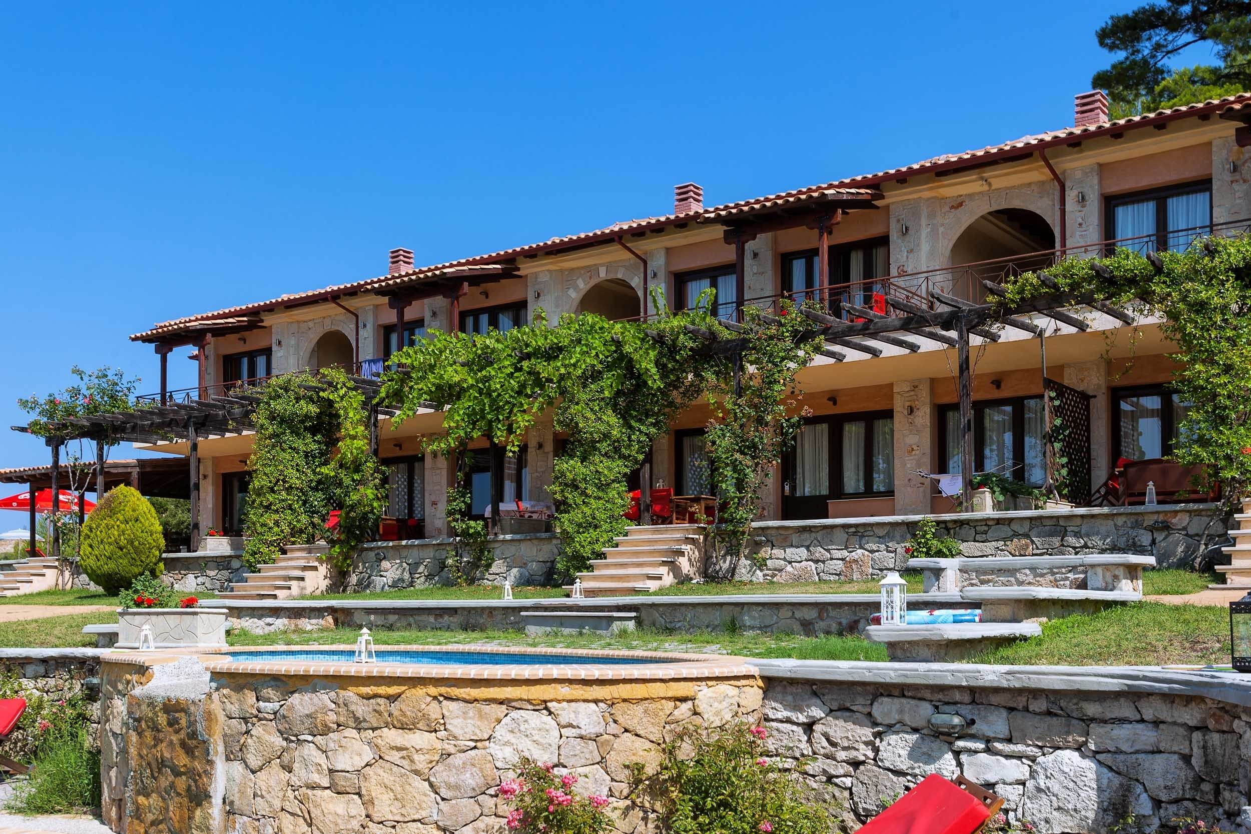 A multi-story building with a stone facade, multiple balconies, and a swimming pool area.