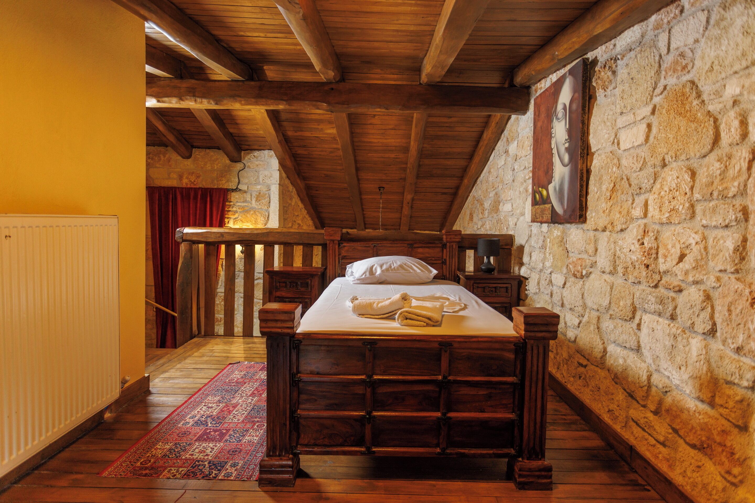 Ein Schlafzimmer mit einem hölzernen Bett, Steinwänden und einer schrägen Decke.