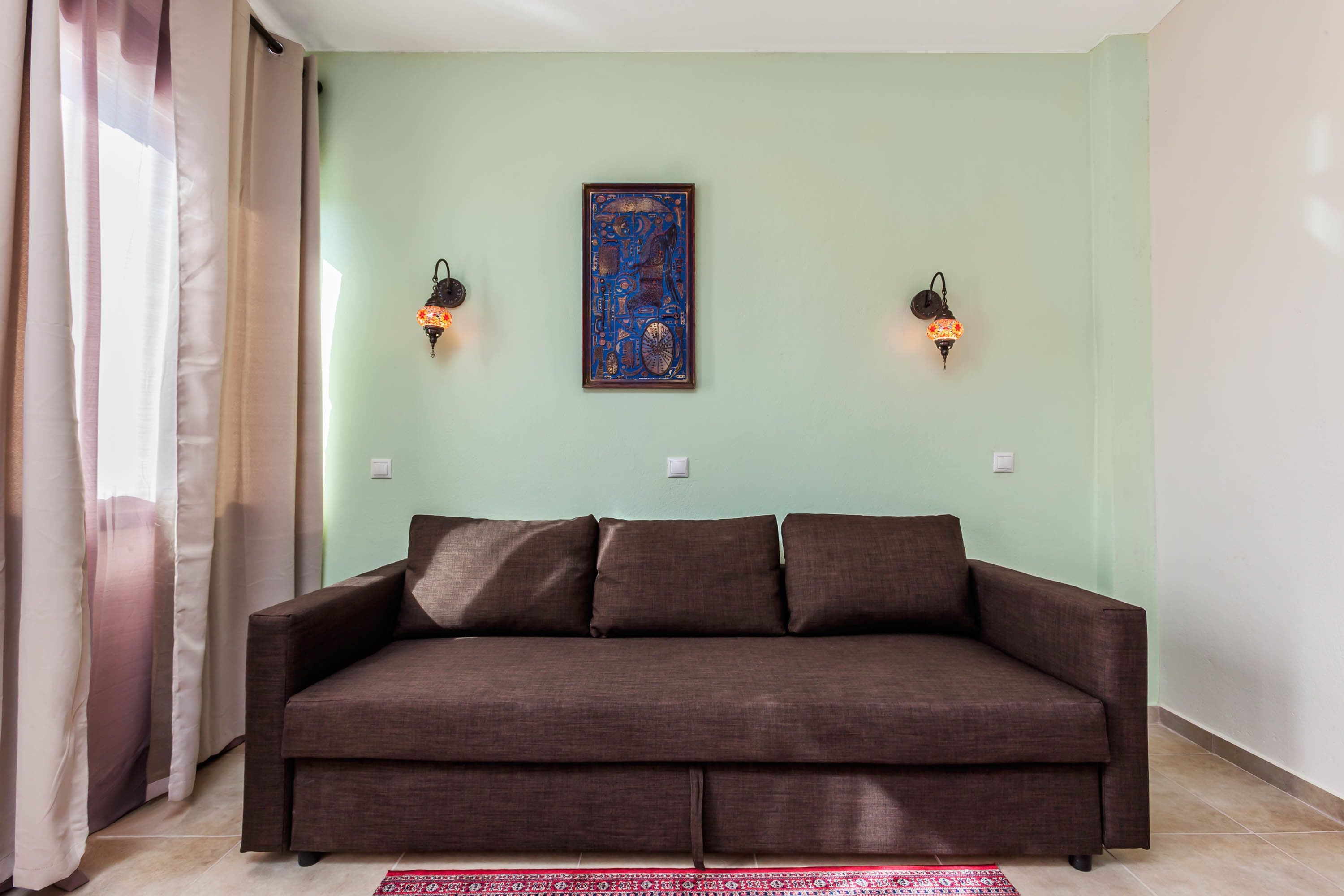 Un sofá marrón frente a una pared verde claro, con dos lámparas de pared y una obra de arte enmarcada.